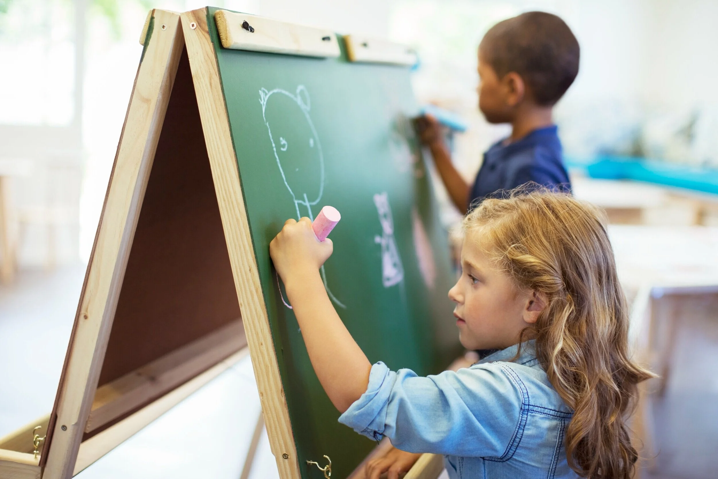 Two children drawing together at a chalkboard easel